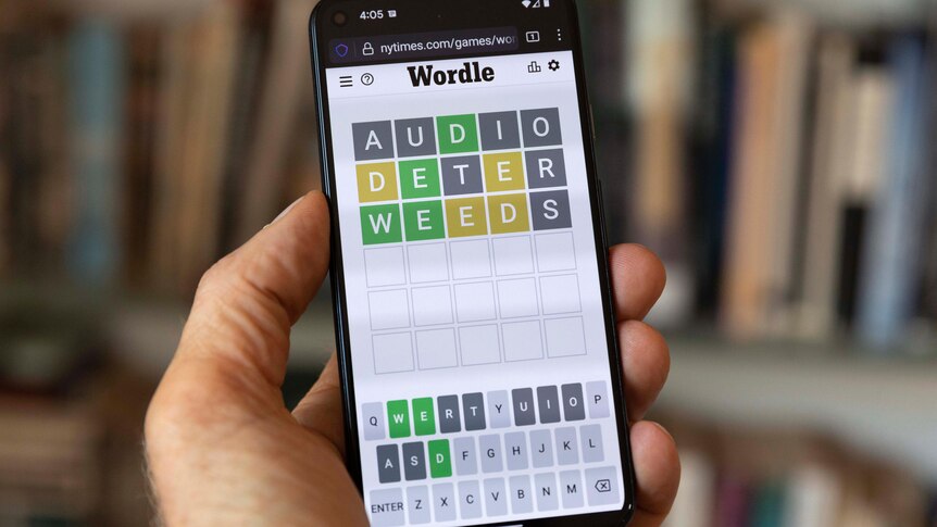 A hand holds up a phone with a Wordle game seen on the screen