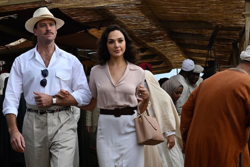 A couple aged in their 30s, wearing light linen clothing, walk arm in arm in a busy Egyptian market