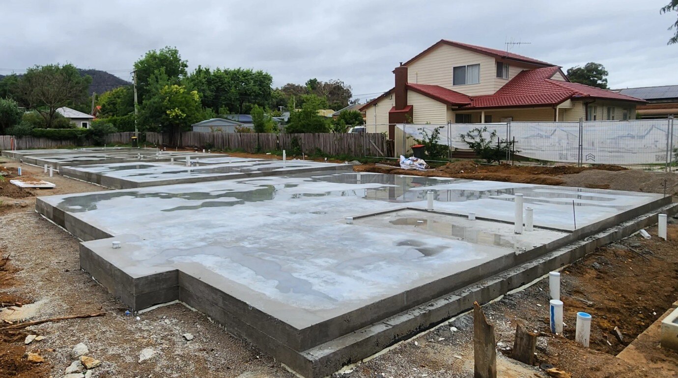 A freshly laid concrete slab on a block with a big house and trees nearby.