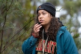 A woman stands in the bush and holds a small microphone near her mouth