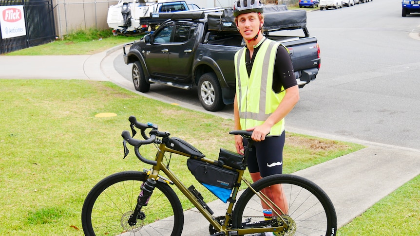 Young man in a yellow hi Vis vest standing beside his bike all packed, helmet on.