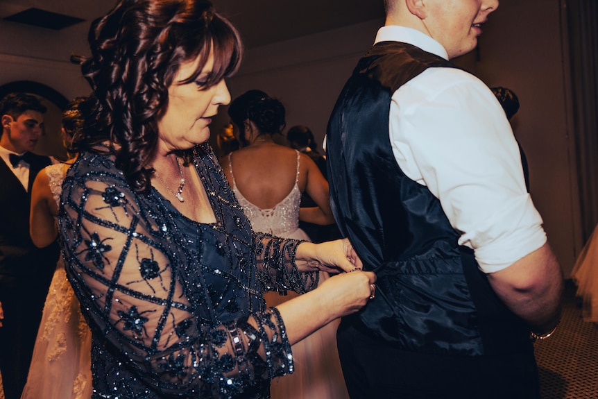 A woman wearing a sequinned top fixed the back of a young man's suit.