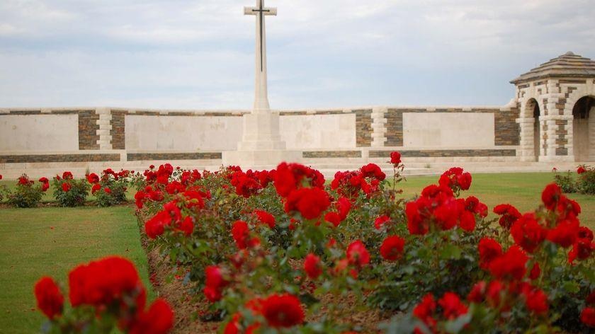 Poppies sit in front of a cross at the WWI memorial at Fromelles