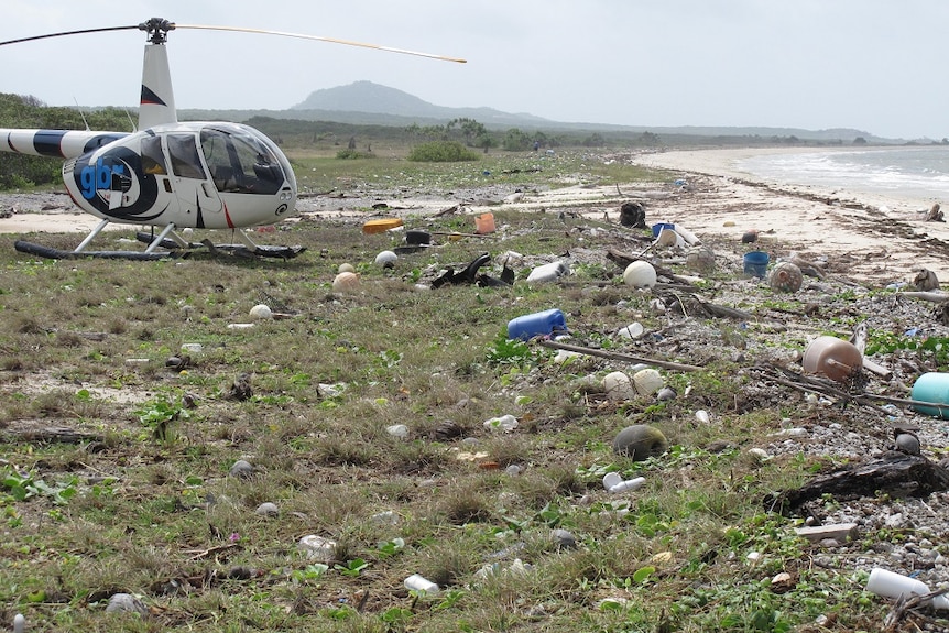 Surrounded by plastic bottles, buoys and other rubbish, a helicopter is parked on a remote far north Queensland beach.
