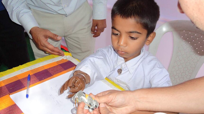 A small boy in Bangalore sits at a desk wearing a prosthetic hand.