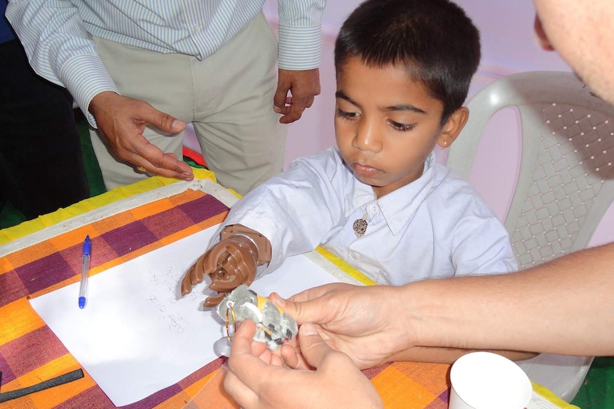 A small boy in Bangalore sits at a desk wearing a prosthetic hand.