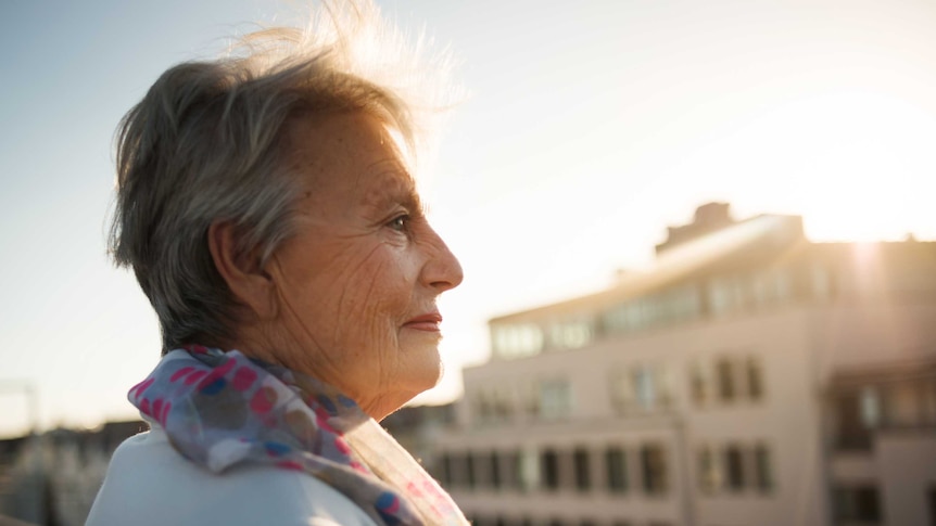 Older woman stands on rooftop smiling.