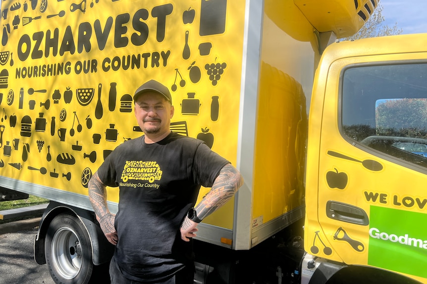 Un trabajador con una camiseta de OzHarvest se encuentra frente a una camioneta de OzHarvest.