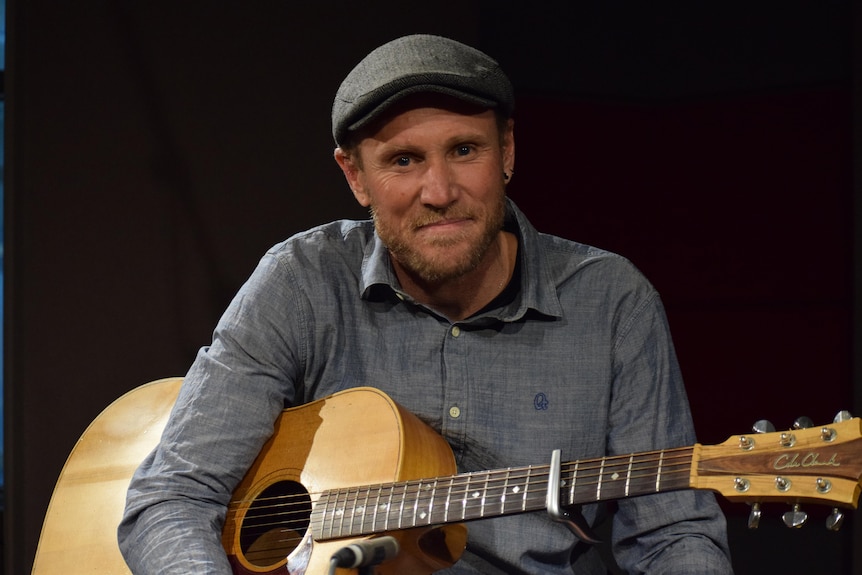 Man sits smiling, holding guitar.