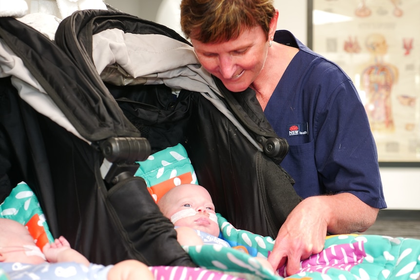 A photo of a wo,man wearing a nurses outfit smiling own at a pram.