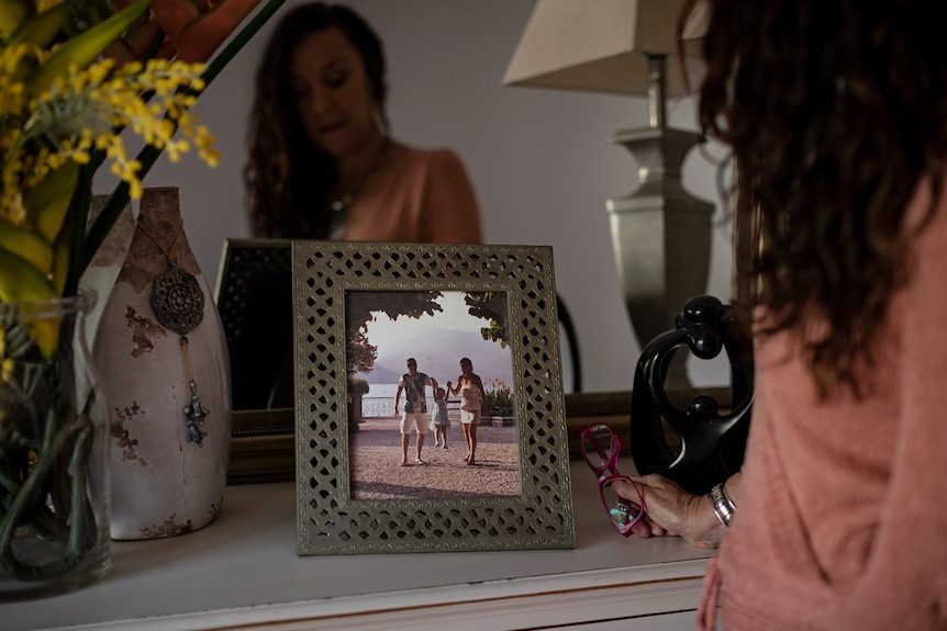 A woman looks at a framed photo of herself with a man and their daughter.