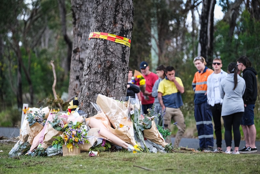 Flowers lay beside a tree in the foreground, while people stand in the distance