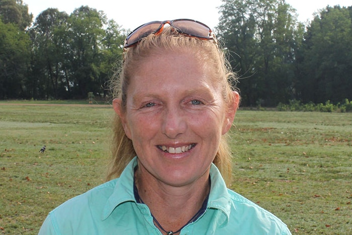 Woman with strawberry blonde hair looks directly at camera with a grass area in the background.