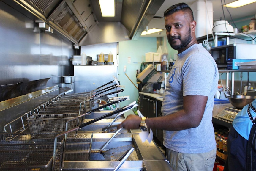 Fish and chip shop owner Shantosh Ramiah stands while cooking at his fryer.