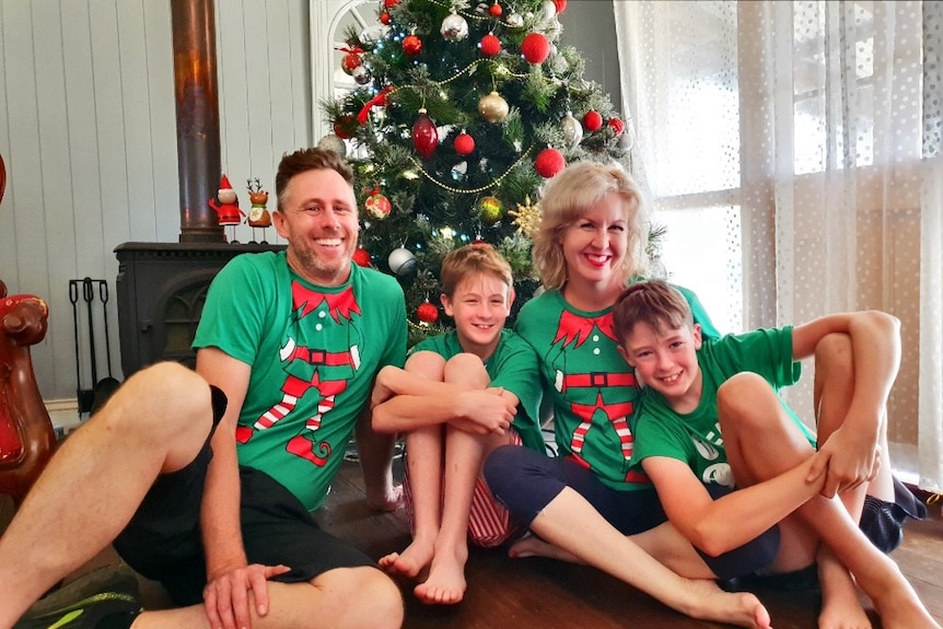 Jody, her husband and her two boys sit underneath a Christmas tree decorated in red and sliver baubles