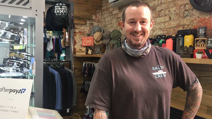 Marcus Stobie standing behind counter of his retail clothing business, register and hats visible.