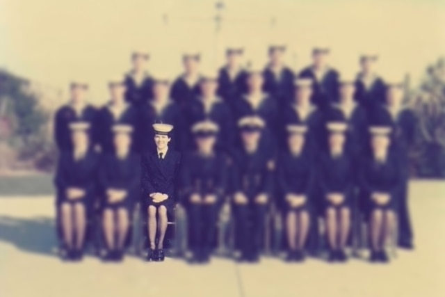 A blurred image shows of a group of navy officers seated for a photo