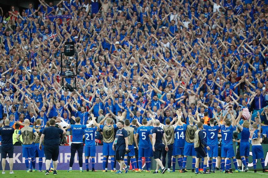 Players line up with their hands up in front of a packed stand of spectators.