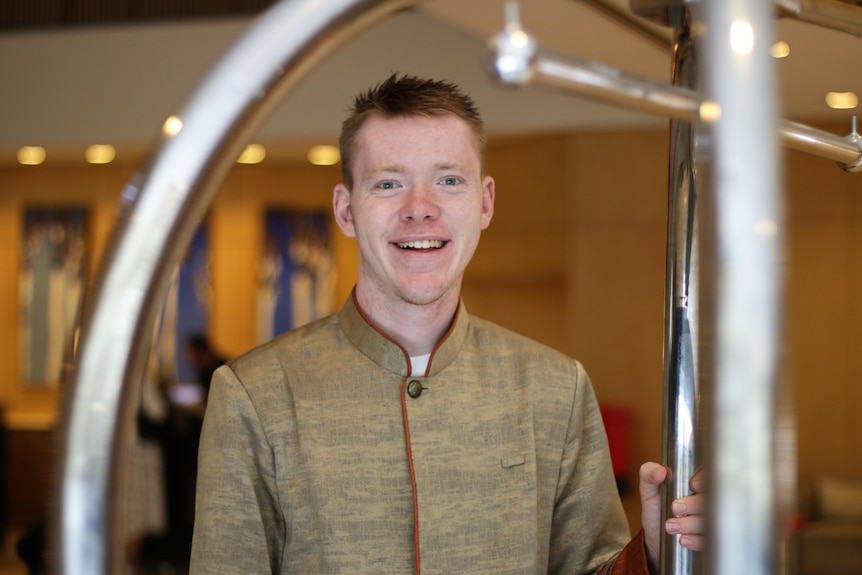 A young white man with short hair working as a bell boy in a hotel lobby 