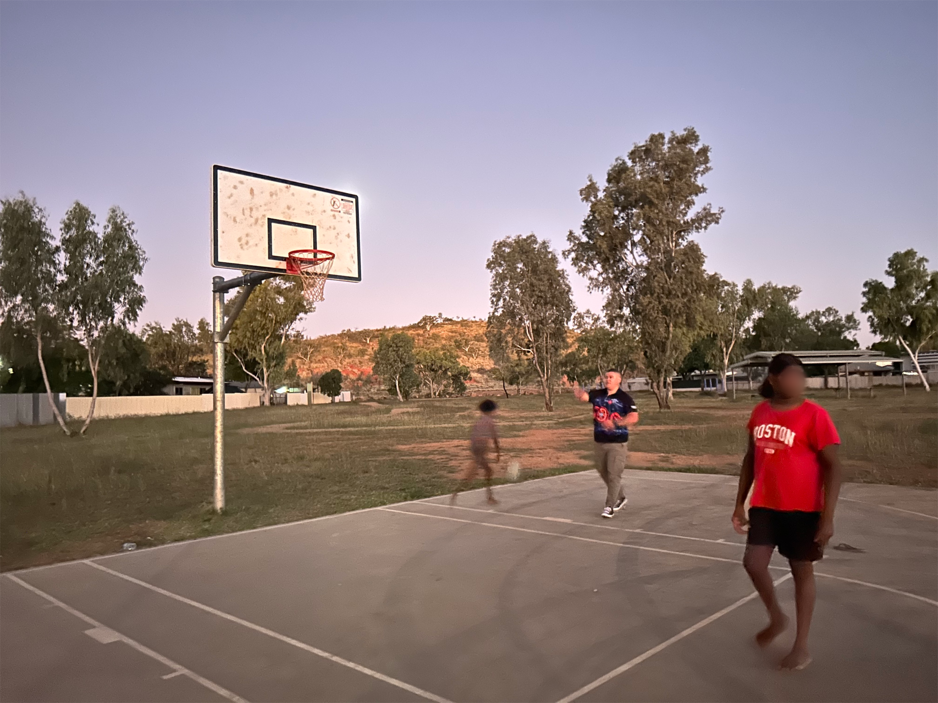 A man and two children play basketball at dusk. 