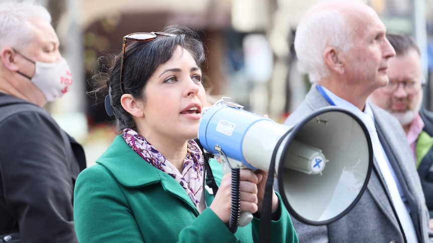 a woman in a green jacket holding a megaphone.