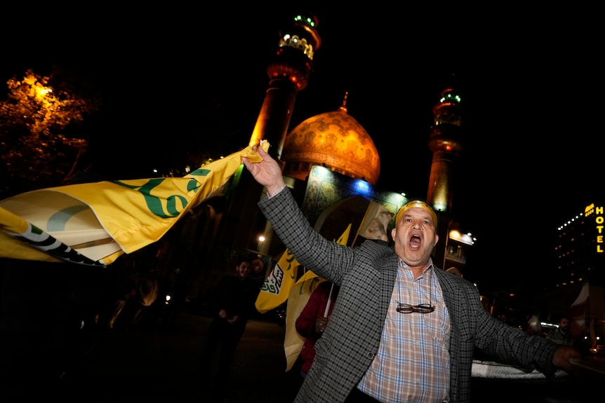 A man chants while waiving a yellow and green flag