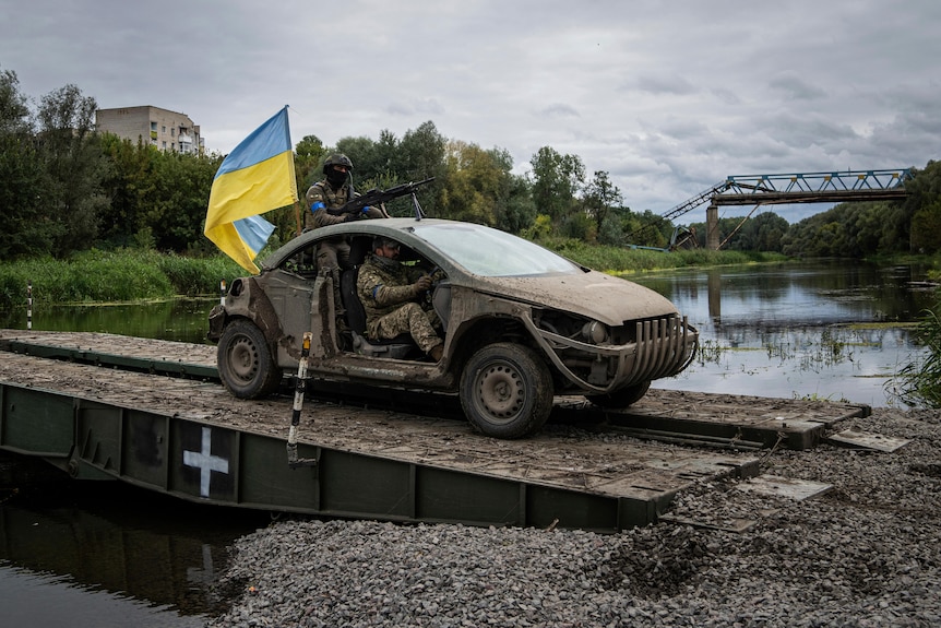 Ukrainian paratroopers drive a vehicle with Ukrainian flag across a bridge.