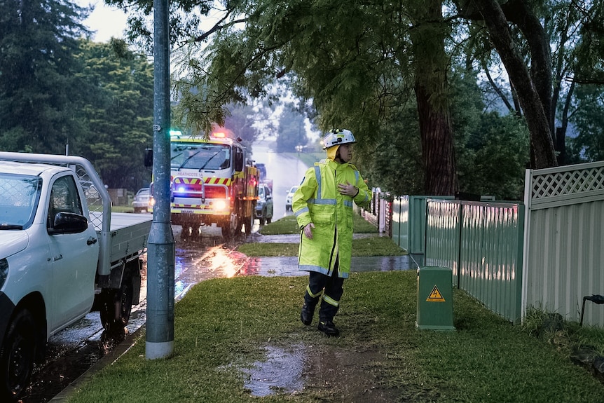 A firefighter walks in the rain and muddy ground with a truck behind him
