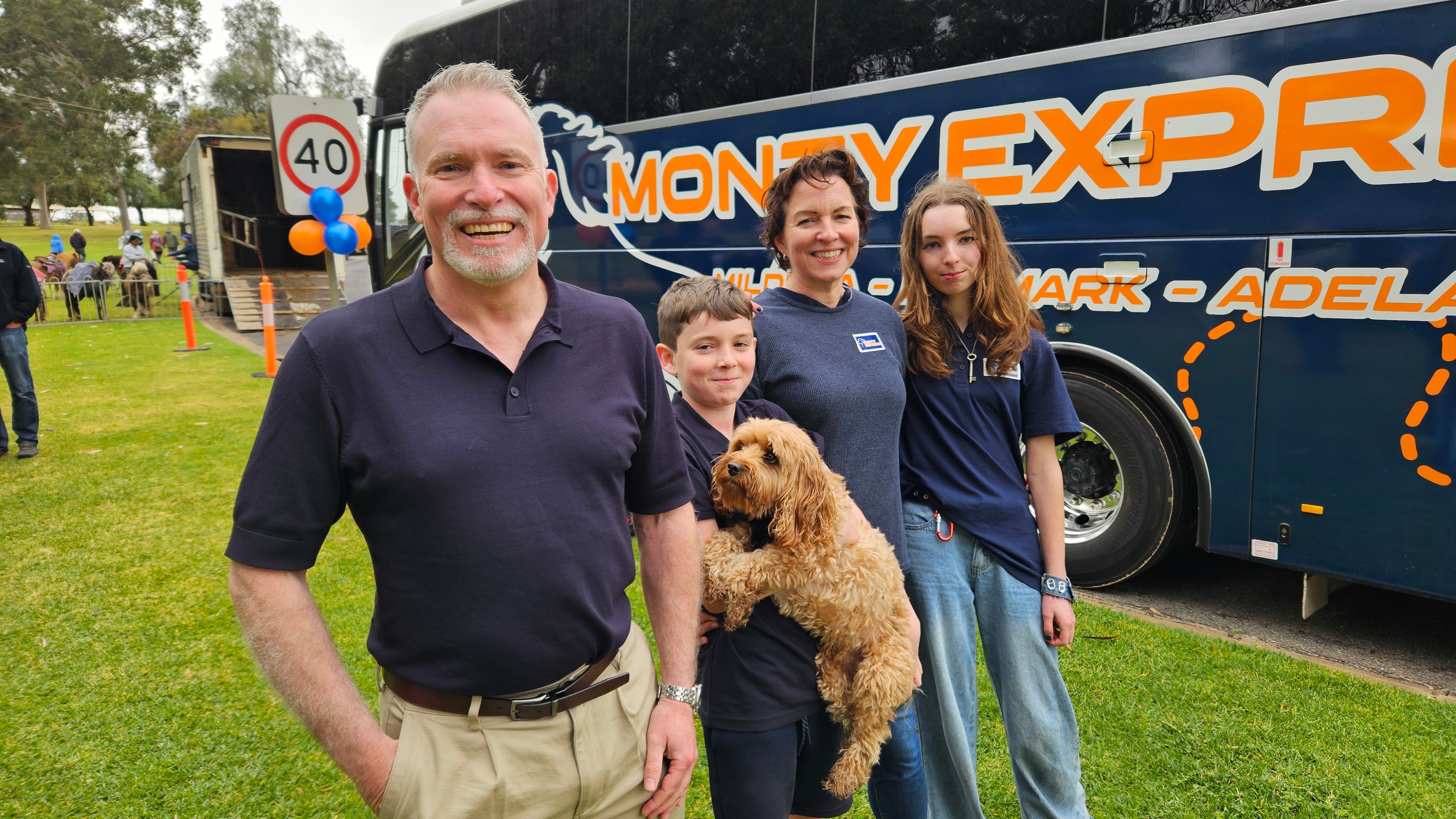 A Caucasian man, his wife, and two children hold a cavoodle, with a bus in the background