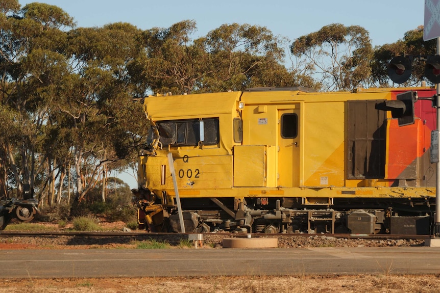 A damaged, yellow freight train engine, motionless in bushland.