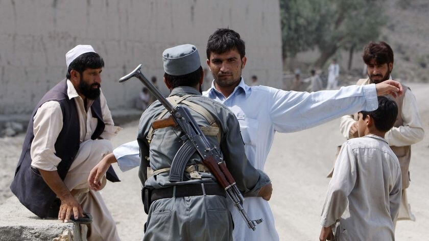 An Afghan policeman searches a local villager in front of a polling station