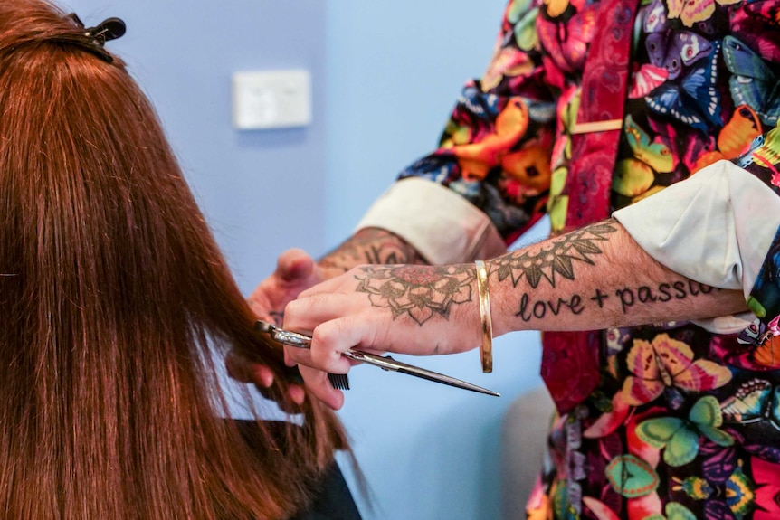 A close up of a man's hands holding scissors while cutting a woman's hair