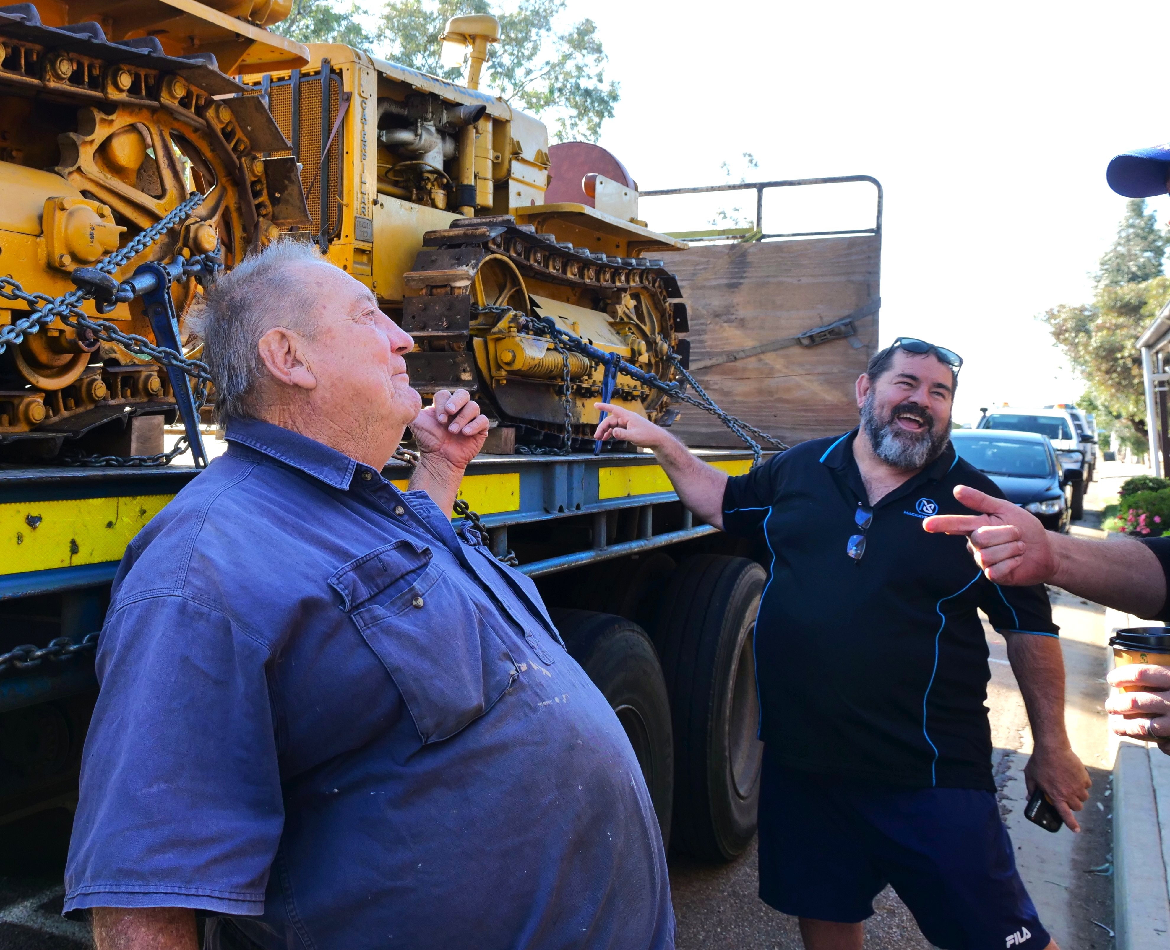 two men gesture towards tractors on the back of a truck