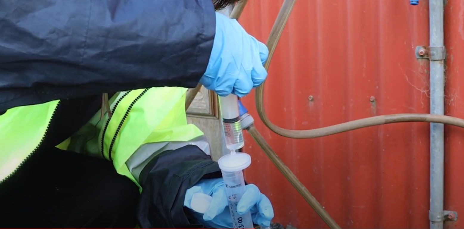Gloved hands syringing water into another syringe next to a tin water tank