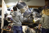 A man throws a large plastic bag full of clothing onto a pile of similar bags.