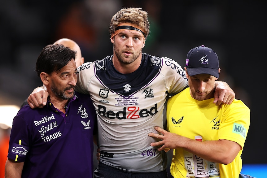 Christian Welch walks with his hands on the shoulders of two men, one either side of him