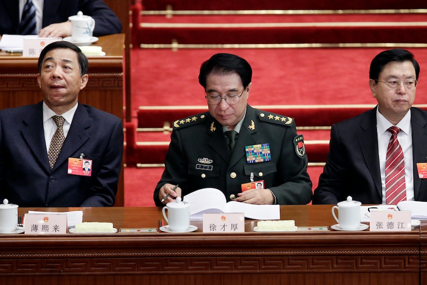 Bo Xilai looking uncomfortable next to two other seated men 