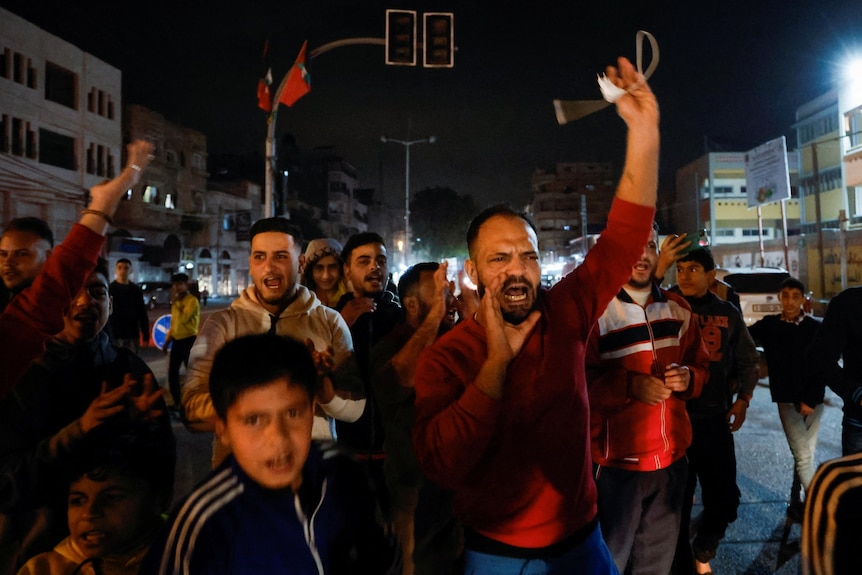 People march along a street at night celebrating by shouting and waving arms in the air.