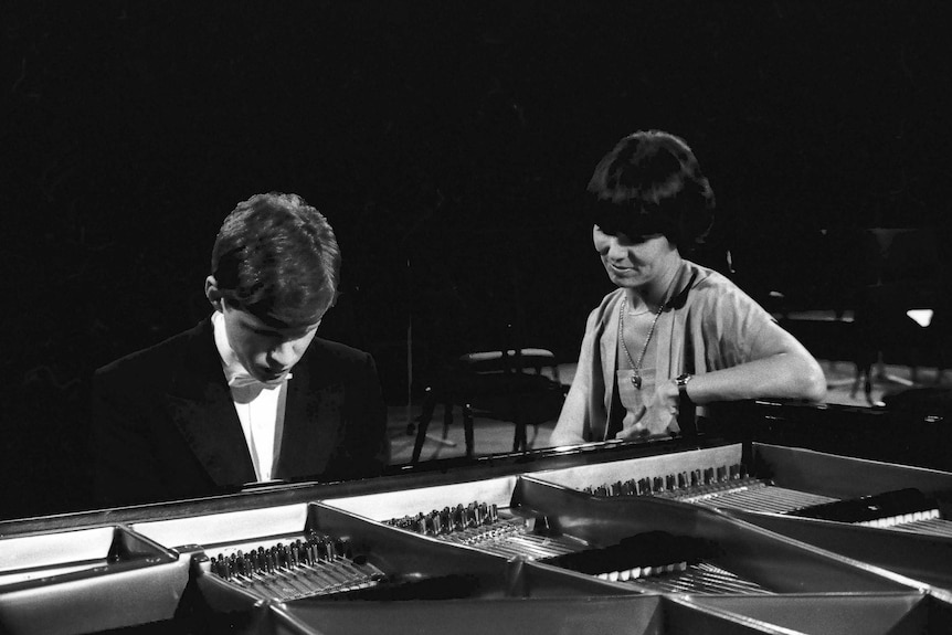 Black and white photo of Margaret Throsby sitting at piano watching pianist Geoffrey Tozer play.