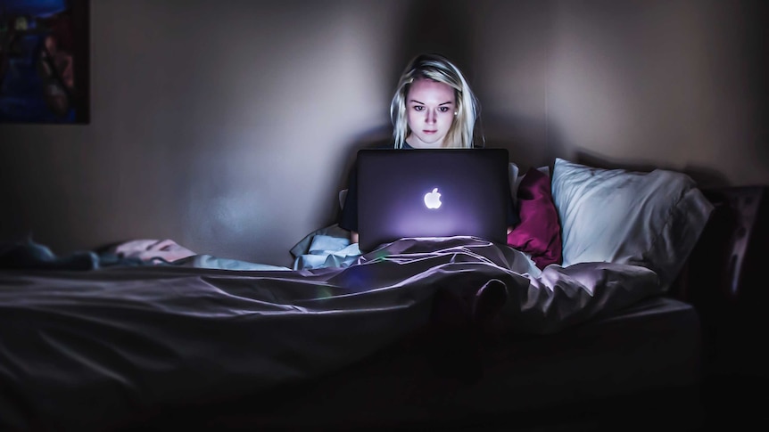 A woman in a bedroom on a laptop.