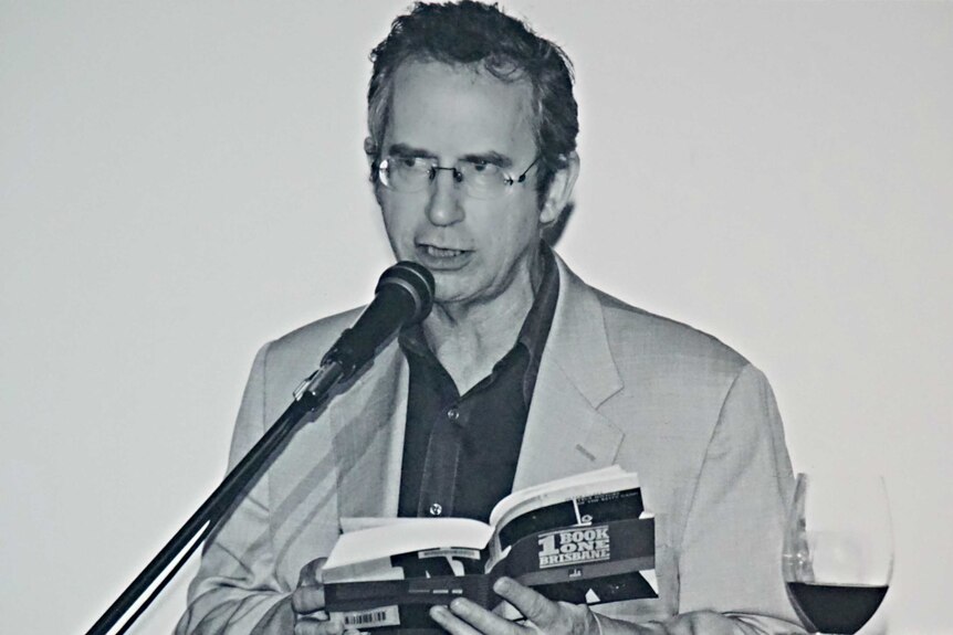 A black-and-white photo of author Peter Carey reading from one of his books.