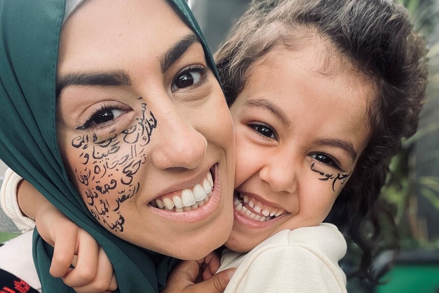 A photo of Aseel (left) wearing a green hijab, with arabic writing on her face, and her daughter (right).