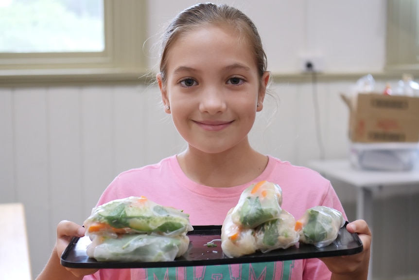 A girl holds a tray of rice paper rolls and smiles at the camera.
