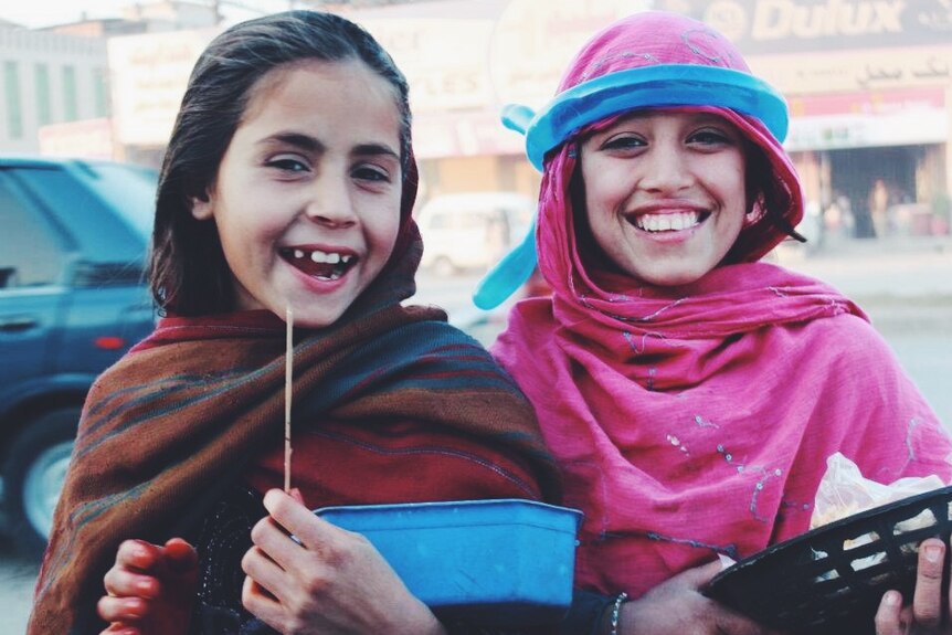 Two Afghan girls, selling products on the street, smile for a photo.