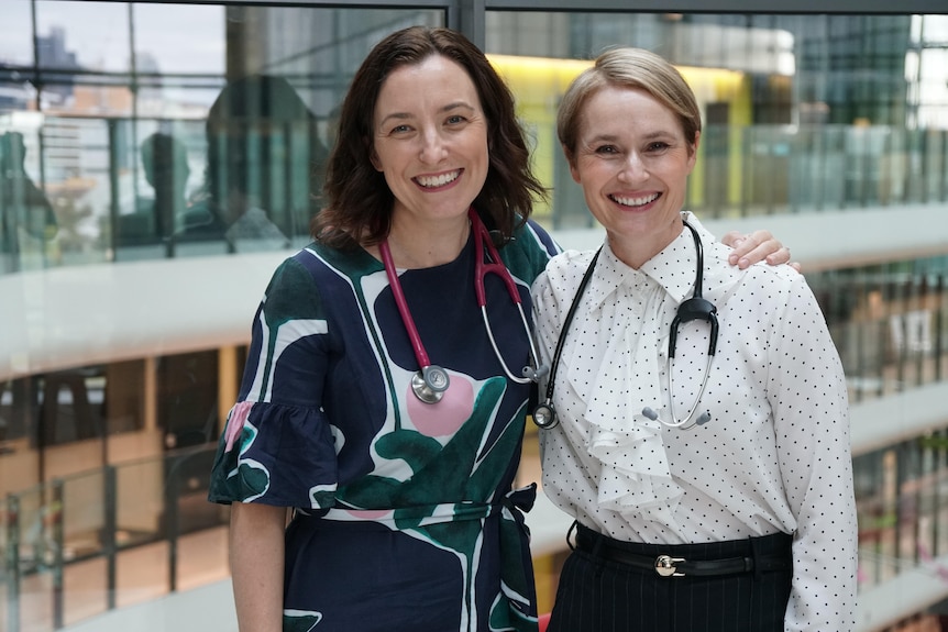 Two women smiling wearing work attire and stethoscopes around their necks