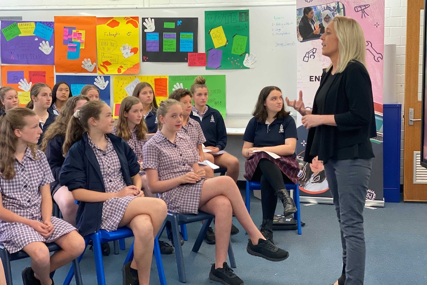 A woman standing up and talking to female school students.