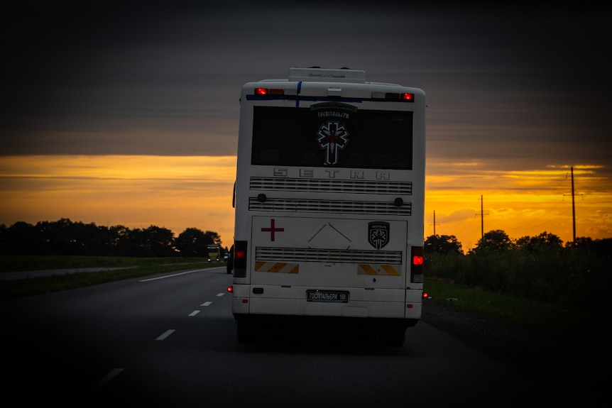 A bus drives on a two-lane road heading towards an orange sunset