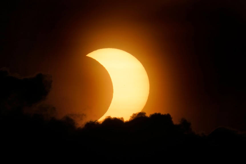 A partially eclipsed sun peaks out from behind a cloud as it rises over lower Manhattan in New York