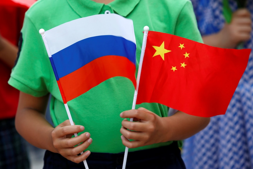 A child in green shirt told two small Chinese and Russian flags