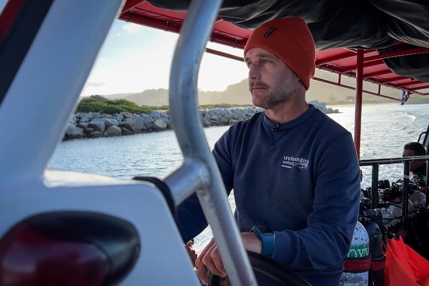 Man wearing a red beanie and navy blue long-sleeved t-shirt steering a boat.